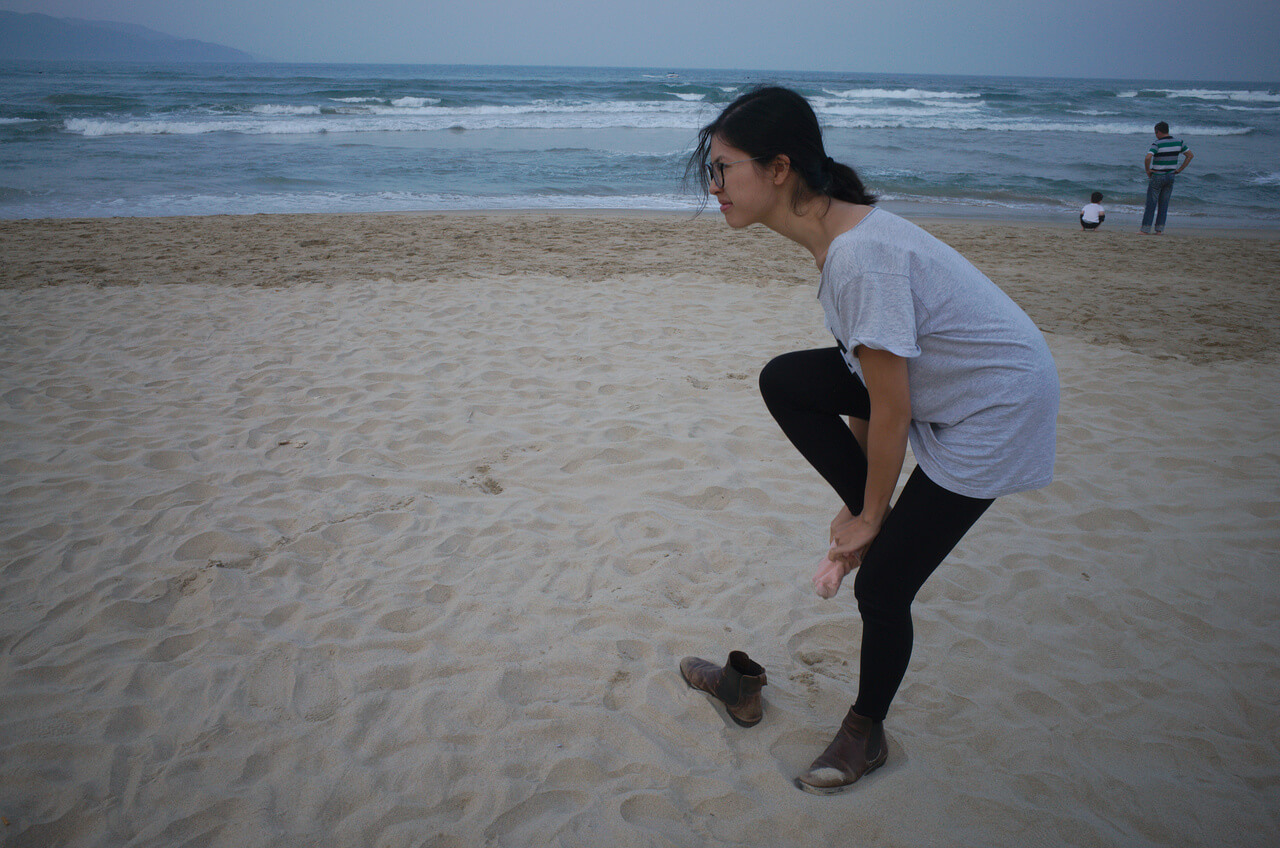 Clara enlève du sable de ses chaussures à la plage de Đà Nẵng