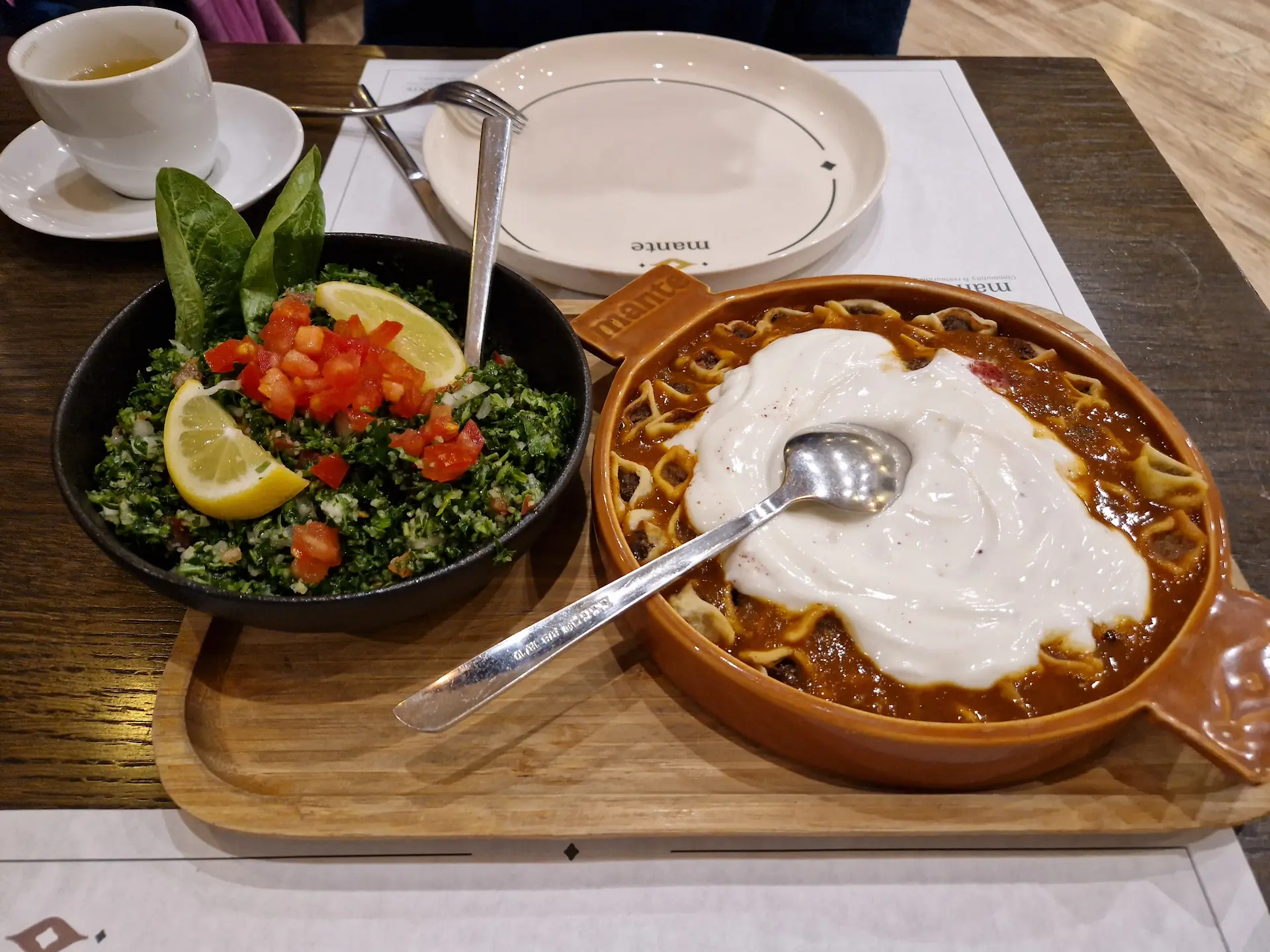 Raviolis arméniens servis dans un plat en terre cuite dans de la sauce tomate et recouvert de yaourt