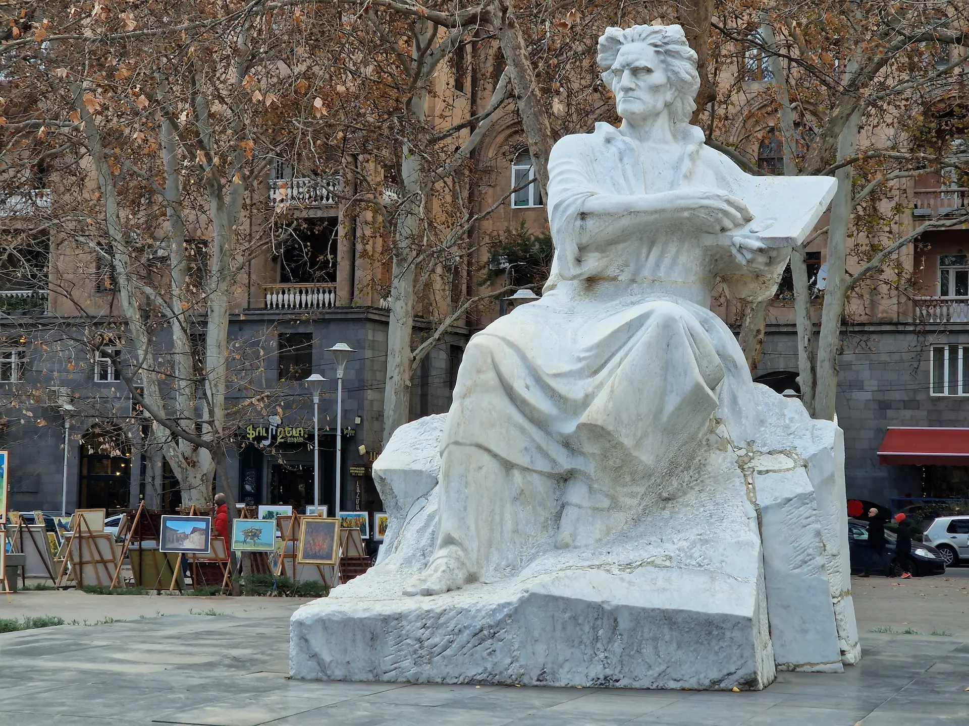 Une statue d'un peintre à l'expression dramatique, assis une toile à la main, les cheveux dasn le vent.