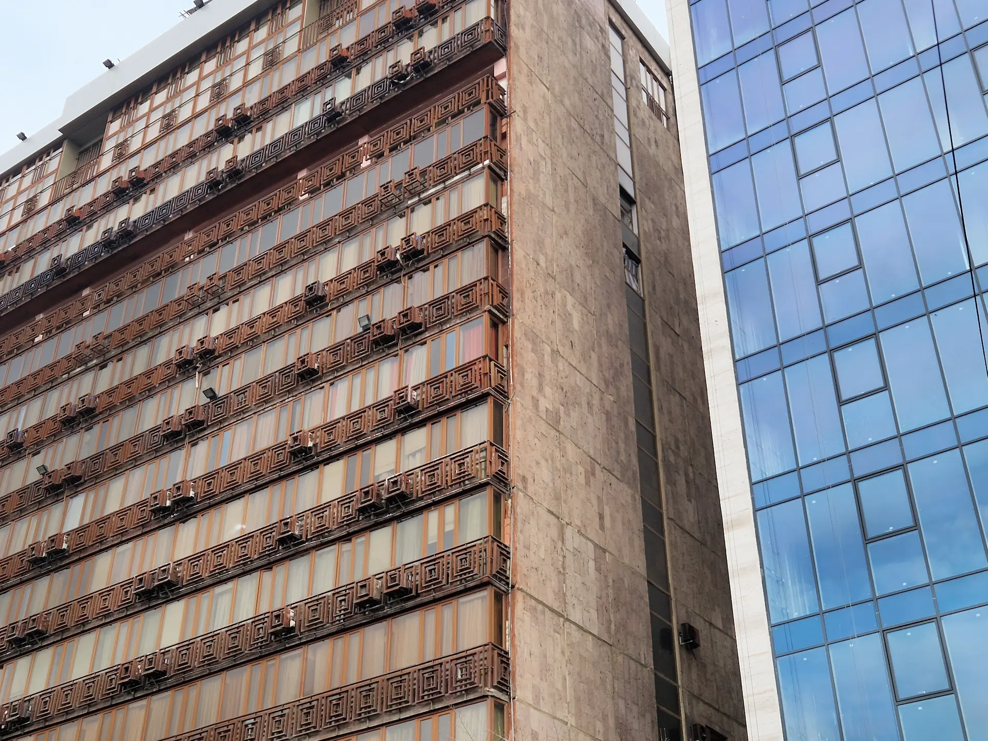 Contraste entre un vieux bâtiment soviétique en pierre brun et son voisin, un immeuble moderne tout en verre.