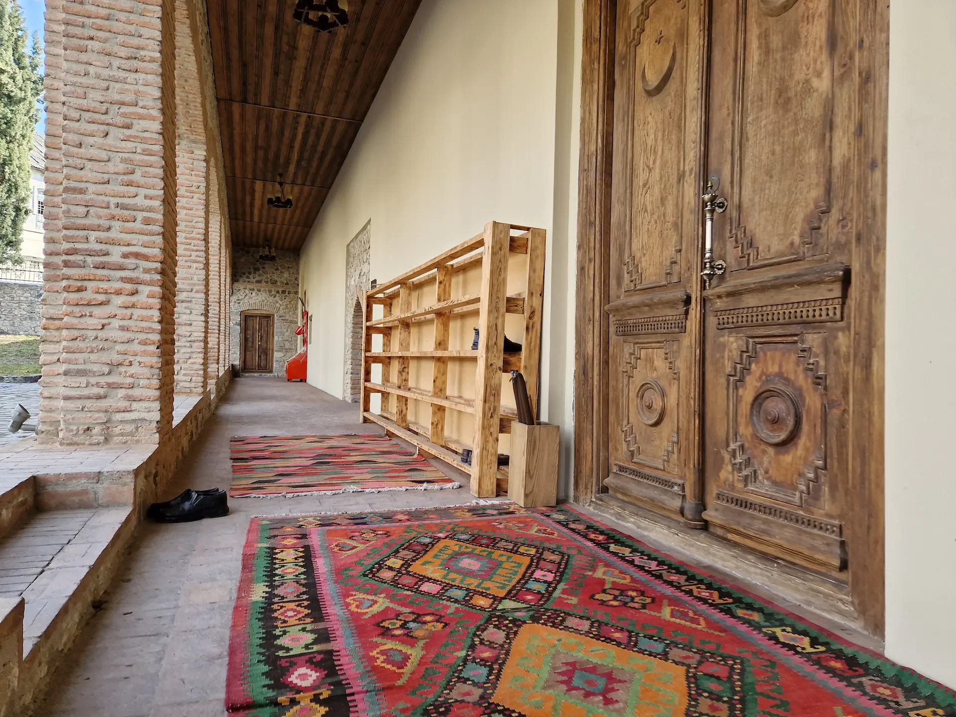 La porte d'entrée de la mosquée en bois. Devant elle, des tapis colorés où les visiteurs peuvent enlever leurs chaussures.