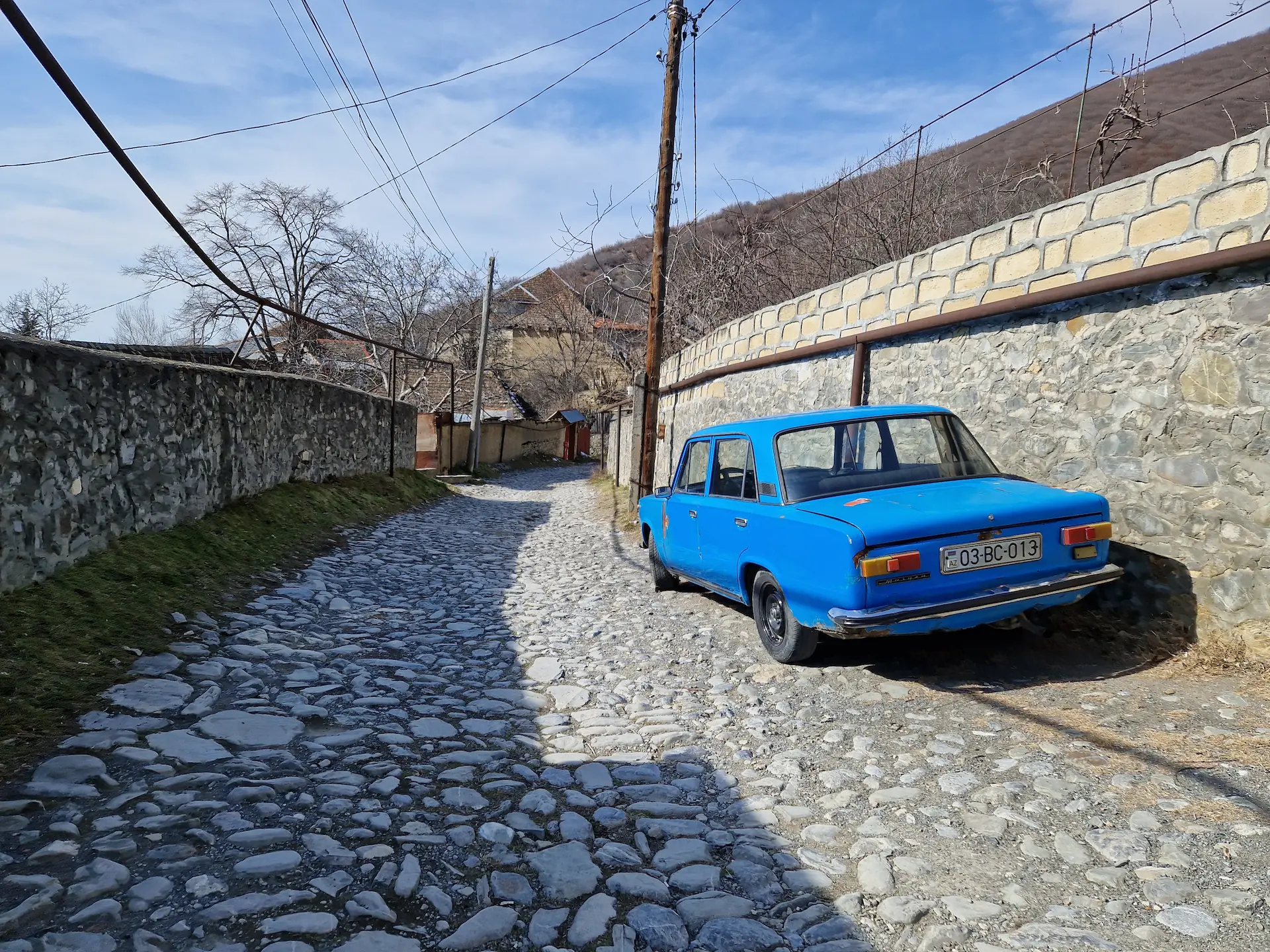 Au détour d'une ruelle, une lada bleue pétante contraste avec les pavés et les murs de pierre. La montagne est juste après le tournant.