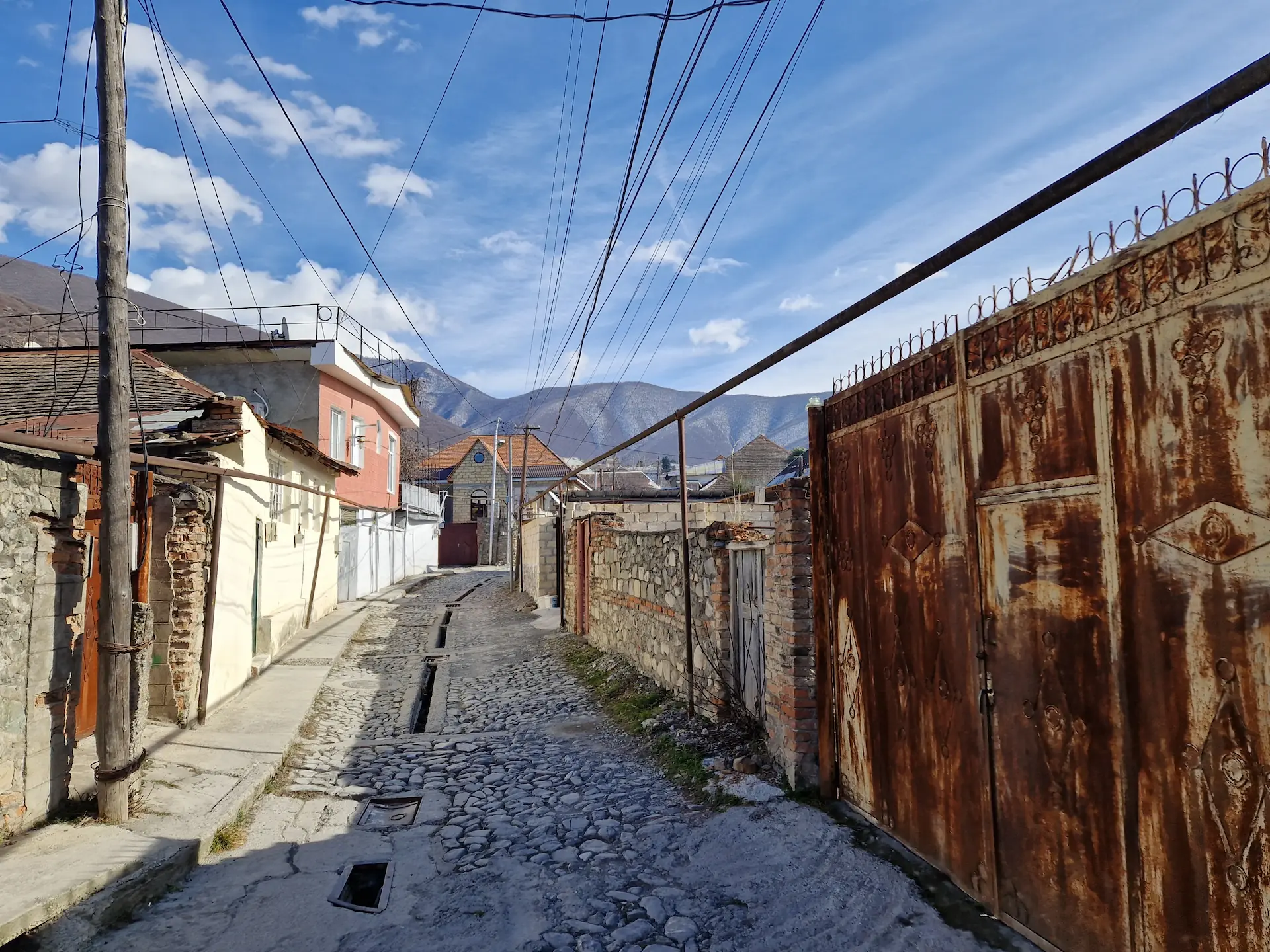 Un vieux portail rouillé dans une ruelle de la vieille ville, les montagnes s'élèvent à l'arrière.