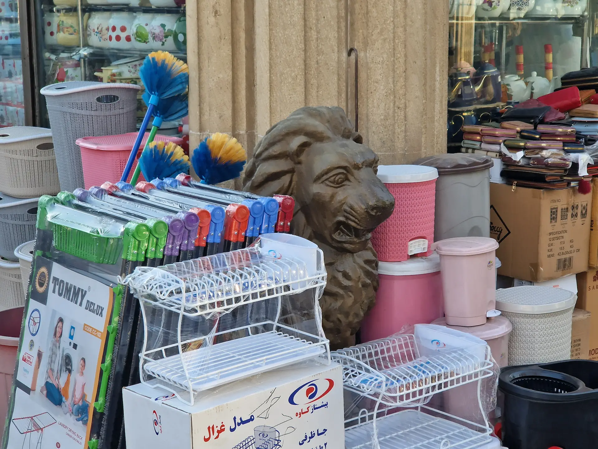 Au marché, une statue de lion est vendue, coincée entre les autres marchandises : poubelles en plastique, étendoir à linge, porte-monnaies, balais.