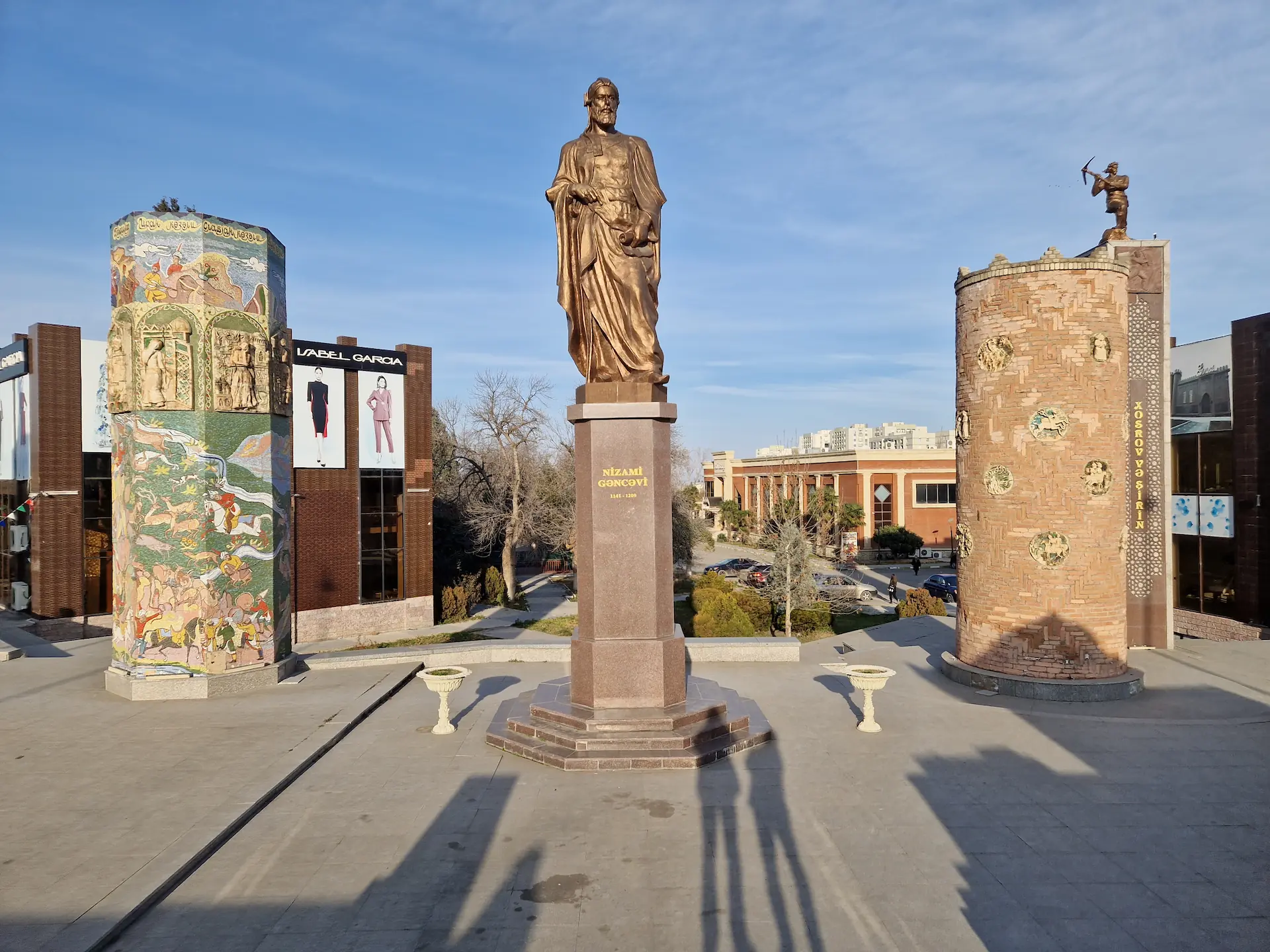 Statue de Nizami entre deux colonnes représentant les histoires de ses poèmes