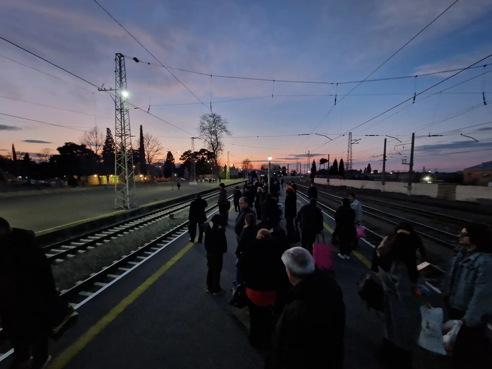 Le quai de la gare est rempli de monde. En fond, le soleil se couche sur Gandja.