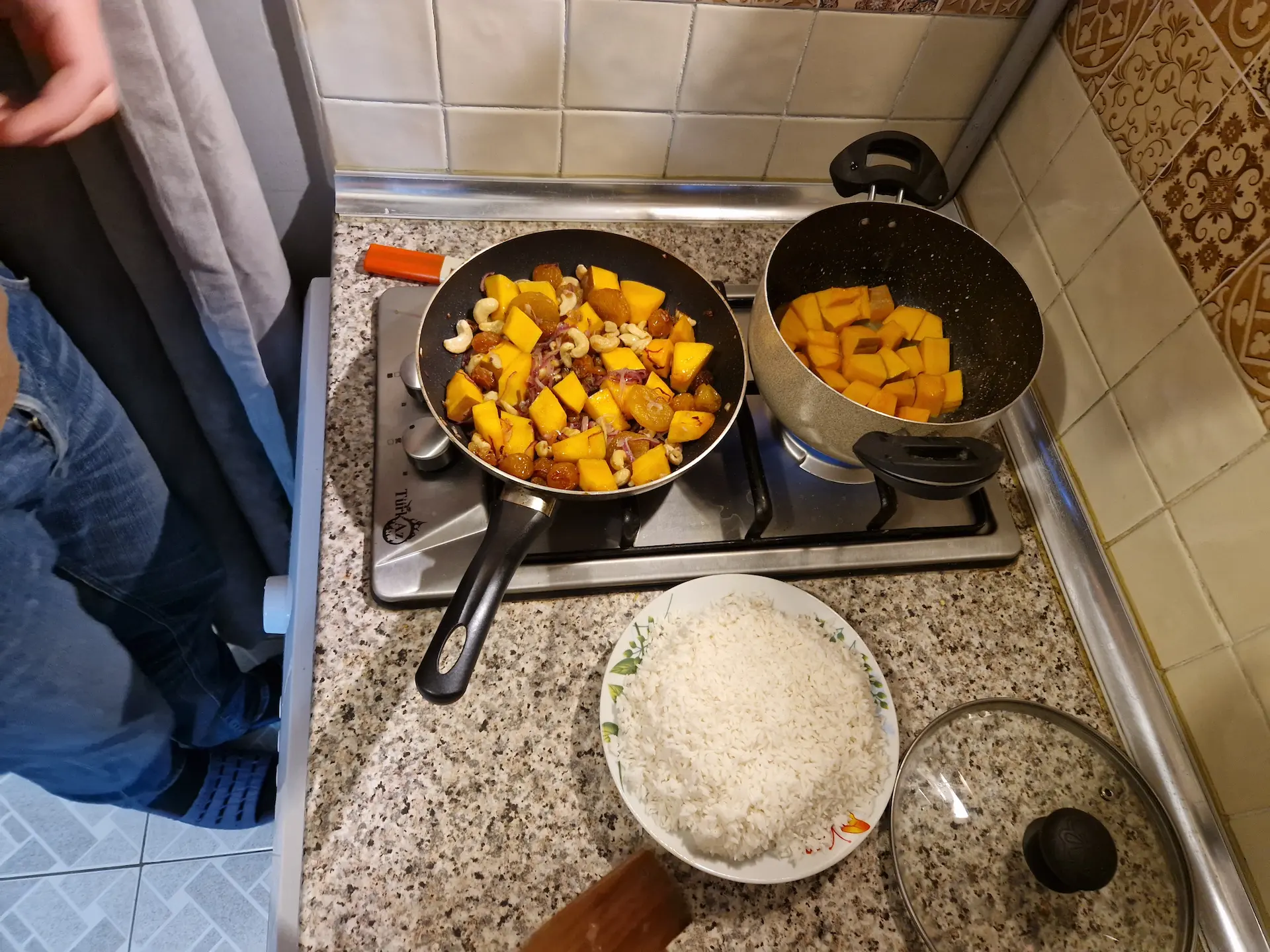 On cuisine un plov à la maison, on est en train de faire revenir de la courge et des fruits secs dans une casserole avant d'y ajouter le riz à moitié cuit, qui finira sa cuisson à la vapeur avec les légumes.