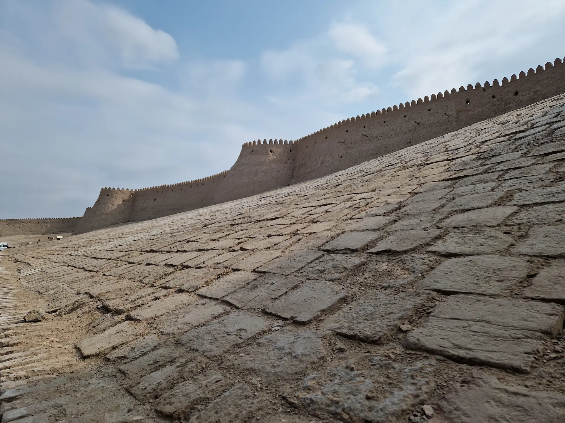 Mur de la forteresse de Khiva vu de l'extérieur. Il est en pierre, dentelé et descend en pente