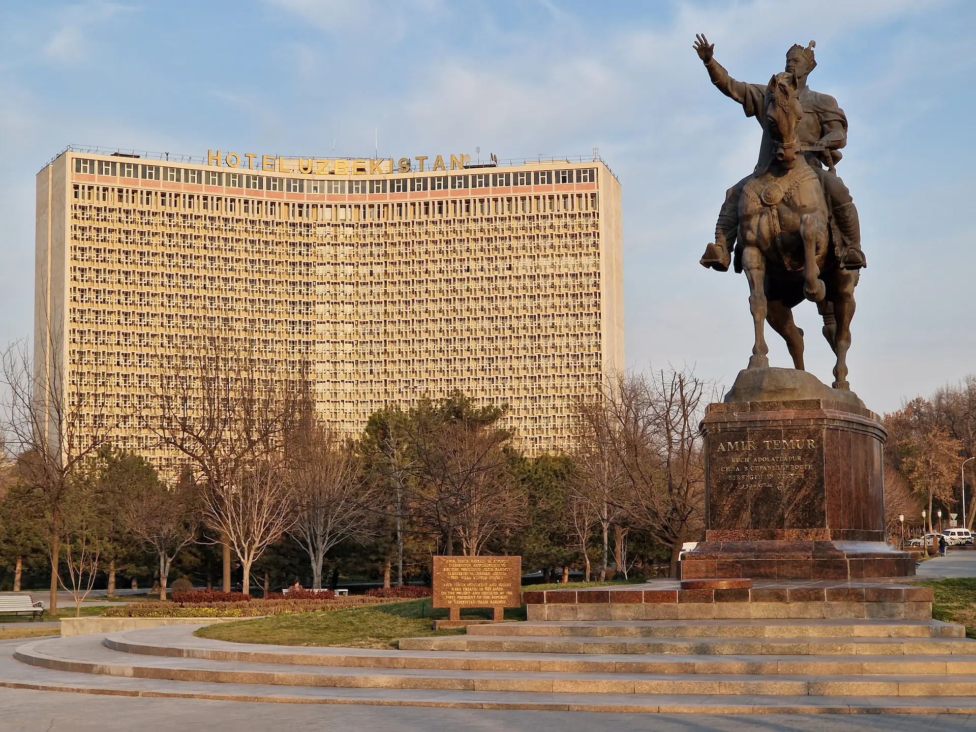 Une statue de Timour à cheval sur le square Timour, et à l'arrière l'hôtel Uzbekistan et sa grande façade brutaliste décorée de motifs de béton