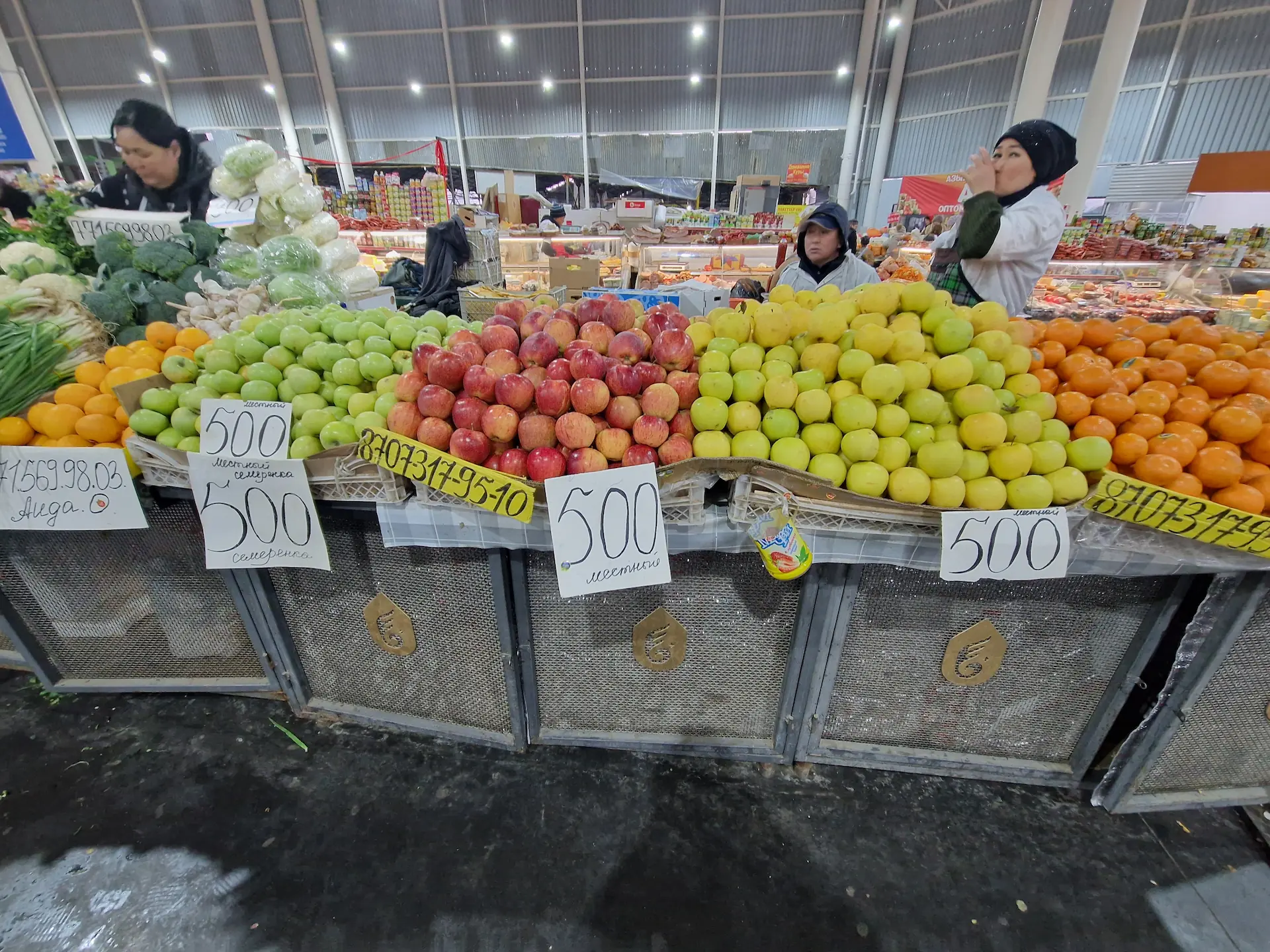 Des dames vendent des pommes rouges, vertes et jaunes.